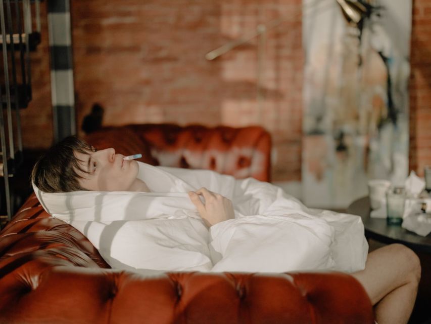 Men with white blanket dan termometer in his mouth