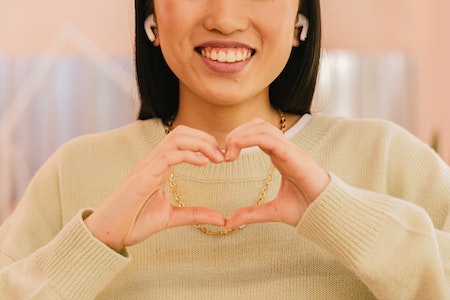 ANTONI SHKRABA Photo by ANTONI SHKRABA: https://www.pexels.com/photo/woman-in-beige-sweater-and-wireless-earphones-smiling-and-showing-heart-shaped-palms-7984964/